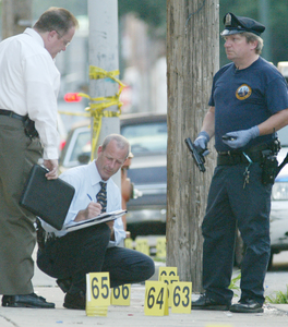 Police recover a gun near Tasker and Taney streets yesterday as investigators log evidence of shots police fired.